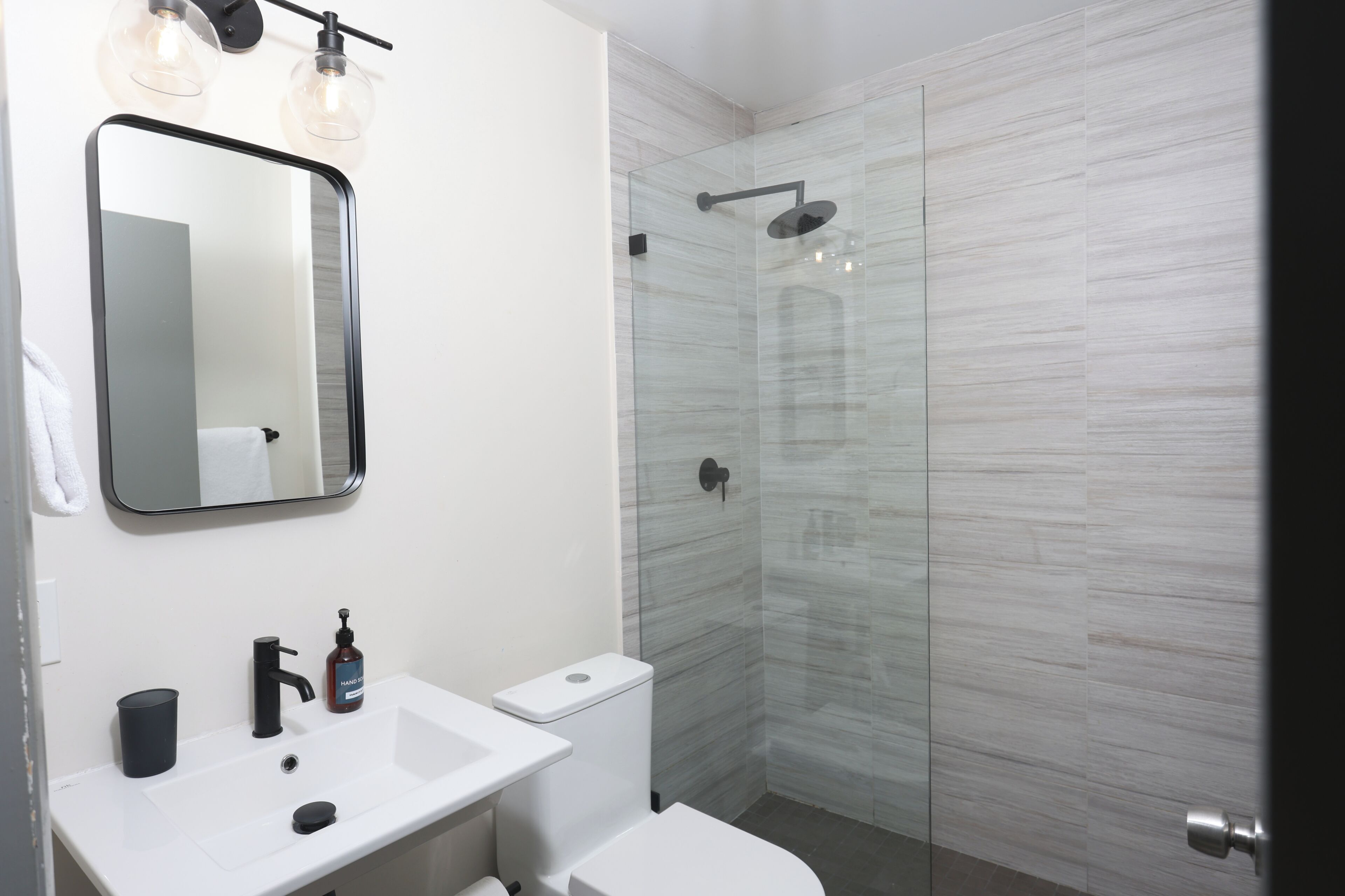 Un baño moderno con lavamanos blanco, grifo negro y cabina de ducha de vidrio.