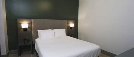 A neatly made bed with white linens, two bedside lamps, and a small table with a plant.