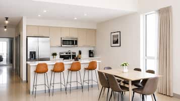 Una cocina moderna con electrodomésticos de acero inoxidable, una isla central con taburetes y una mesa de comedor con sillas.
