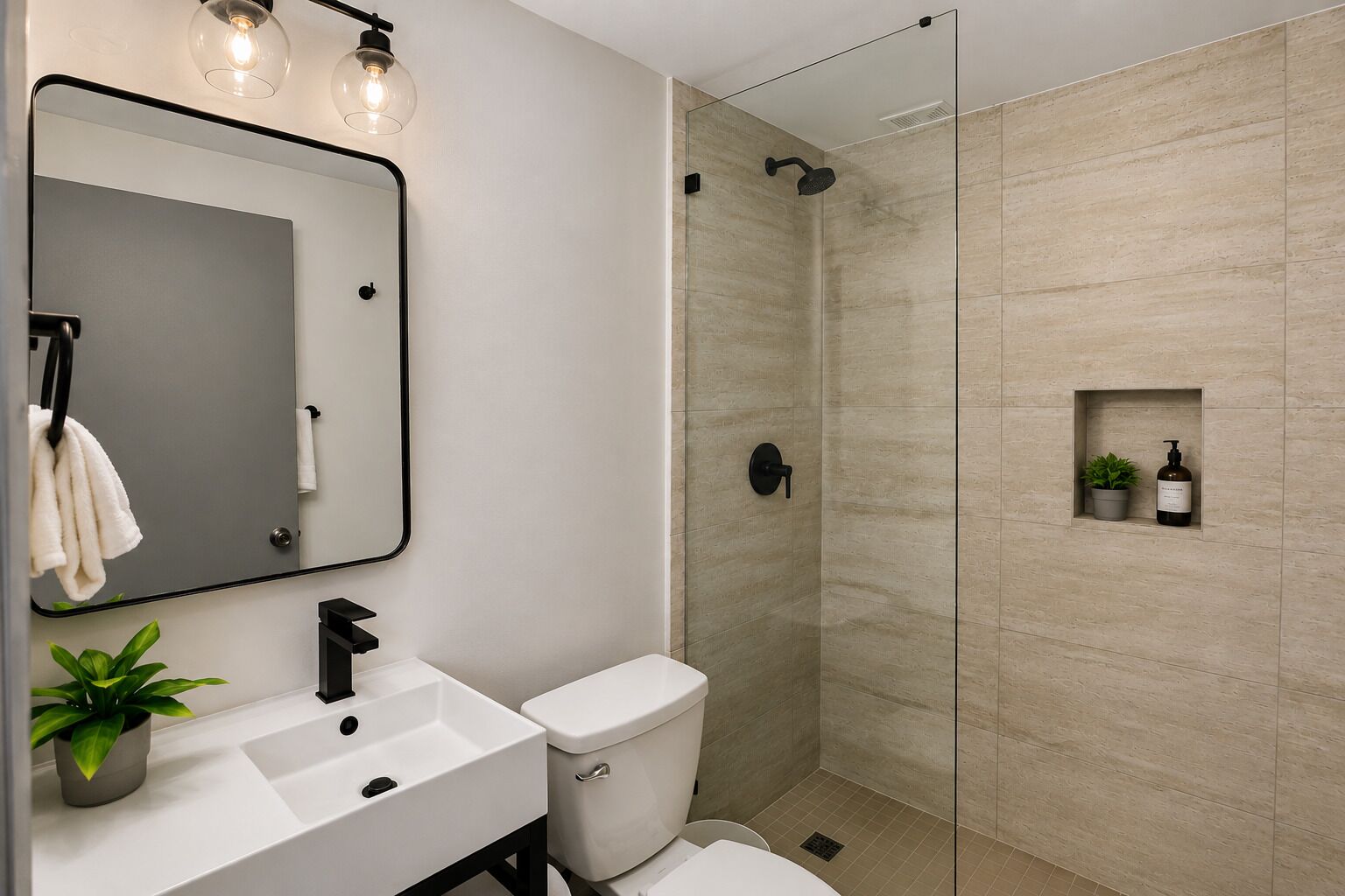 Un baño moderno con cabina de ducha de vidrio, un lavamanos blanco, un inodoro y un espejo con luces colgantes.