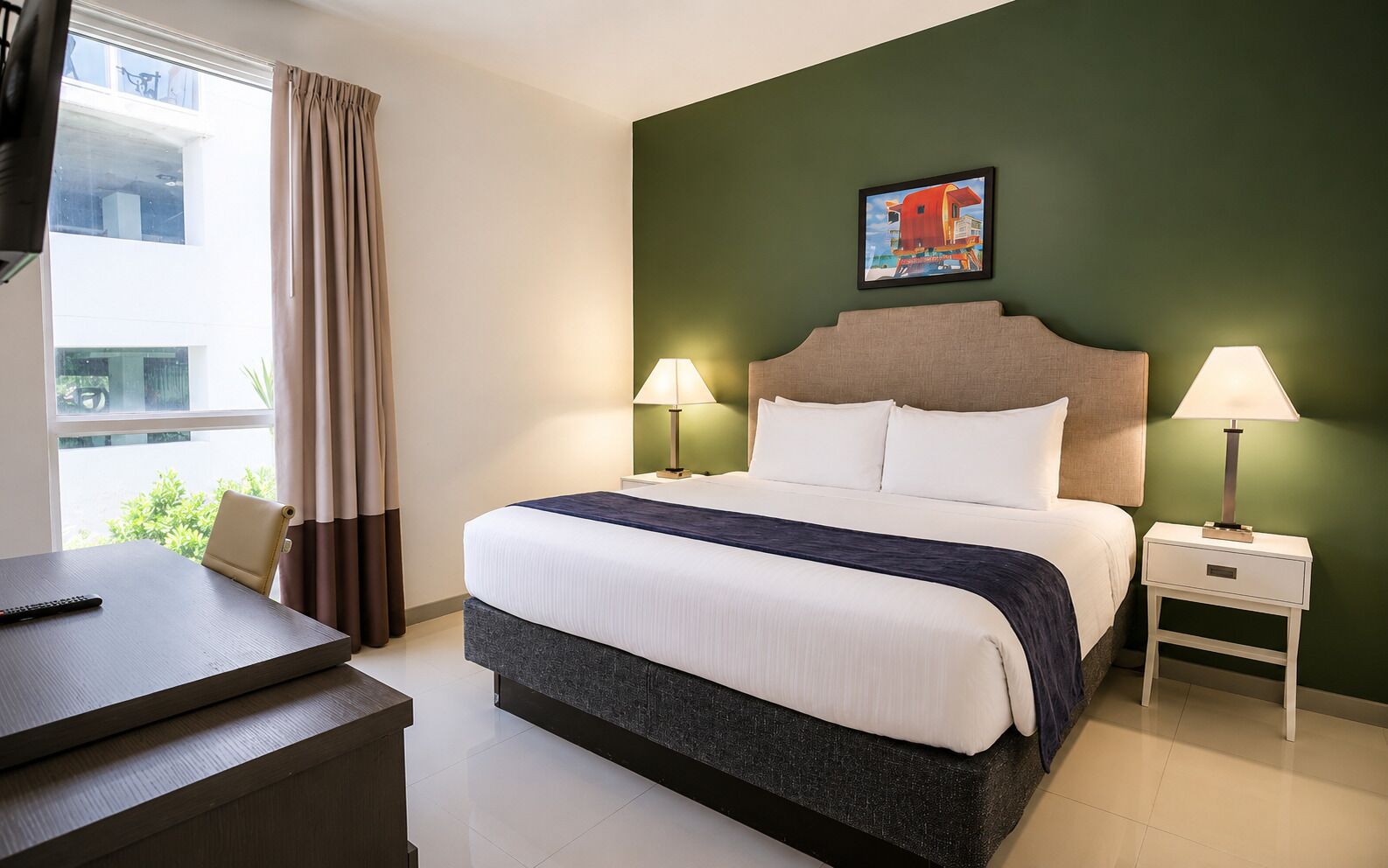 Habitación de hotel con cama, dos mesitas de noche con lámparas, un escritorio con control remoto y una ventana con cortinas.