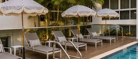 A poolside area with lounge chairs, striped umbrellas, and a clear blue pool.