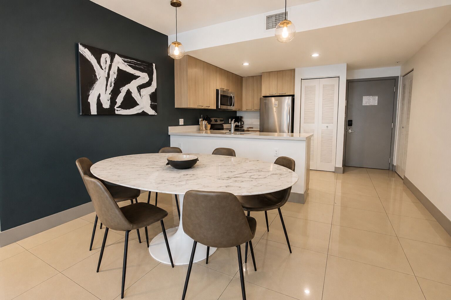 Une cuisine moderne dotée d’un îlot central, d’un coin repas avec une table ronde et d’un tableau abstrait en noir et blanc accroché au mur.