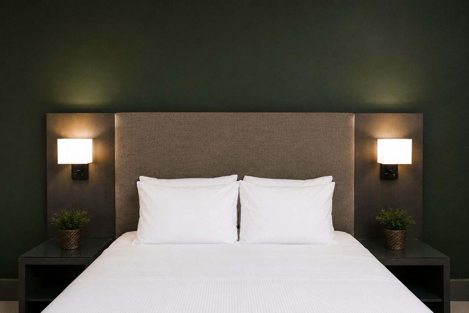 A bed with white linens, two nightstands with wall-mounted lamps, and small potted plants on each side.