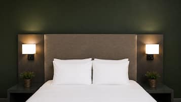 Una cama con sábanas blancas, dos mesitas de noche con lámparas de pared y pequeñas macetas con plantas a cada lado.