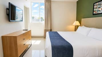 Een hotelkamer met een bed, een tv die aan de muur hangt, een dressoir, een raam met gordijnen en een lamp.