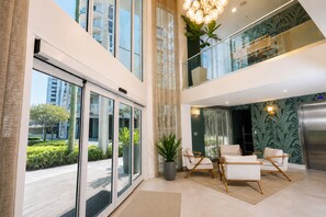 Un moderno vestíbulo con puerta de vidrio, zona de estar con dos sillas, planta en maceta y lámpara decorativa.
