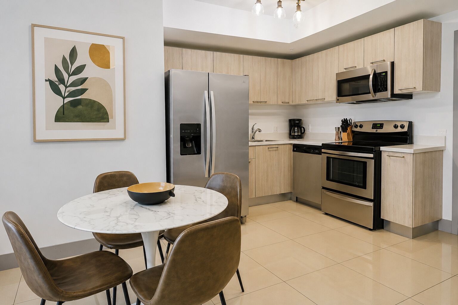 A modern kitchen with stainless steel appliances, a marble table, and brown leather chairs.
