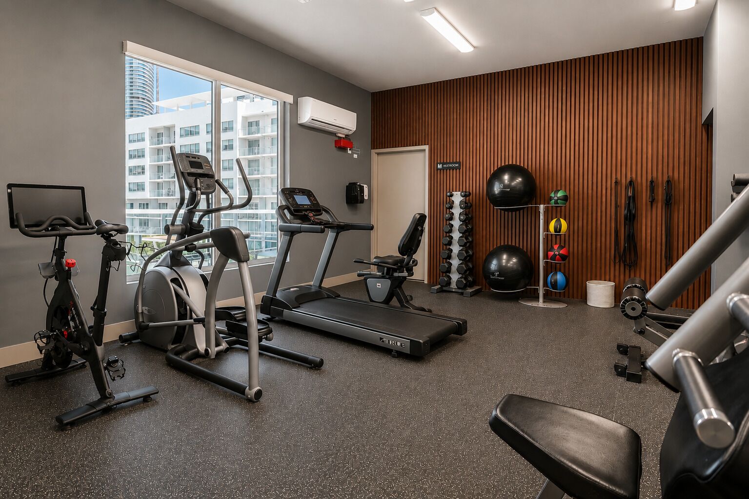 A modern gym with treadmills, an elliptical, a stationary bike, and free weights.