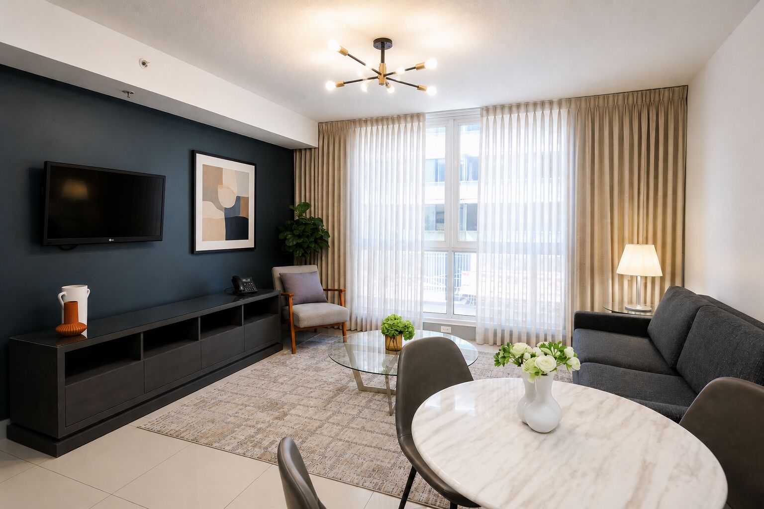 A modern living room with a flat-screen TV, a sofa, a coffee table, and a dining area with chairs.