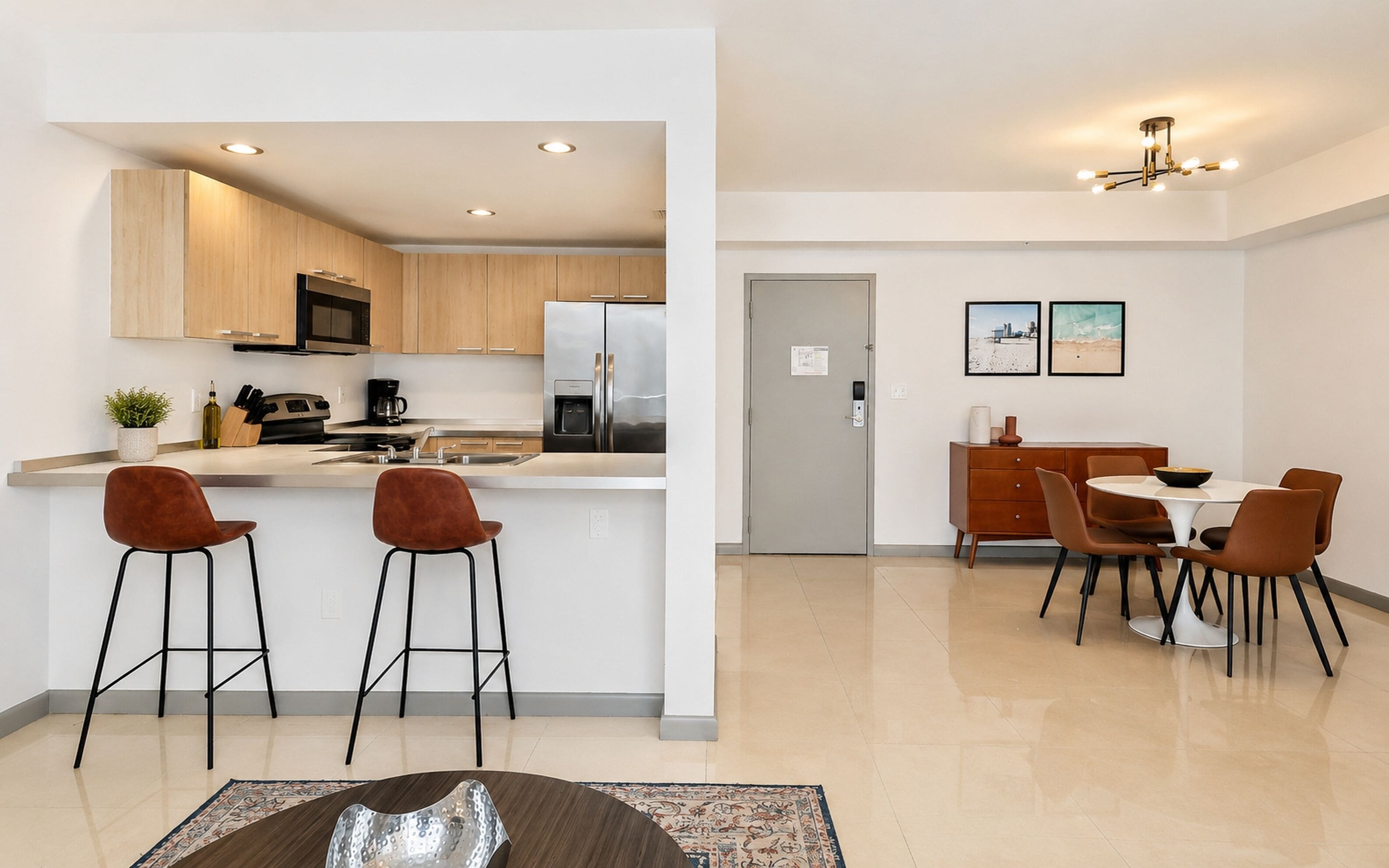 A modern kitchen with wooden cabinets, a stainless steel refrigerator, and a bar area with stools.