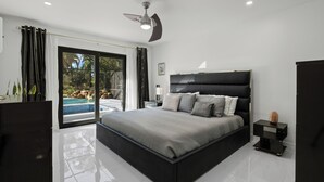 A modern bedroom with a large bed, a ceiling fan, and a view of a swimming pool. - 6 bedroom Oasis with Extra Large Pool, spa, EV Charger & Guest House, Sleeps 16+ (Naples)