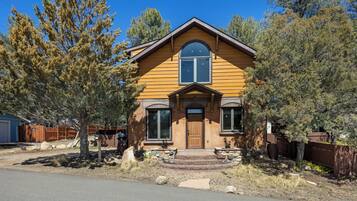 A two-story house with a brown wooden exterior, a front porch, and a stone foundation.
