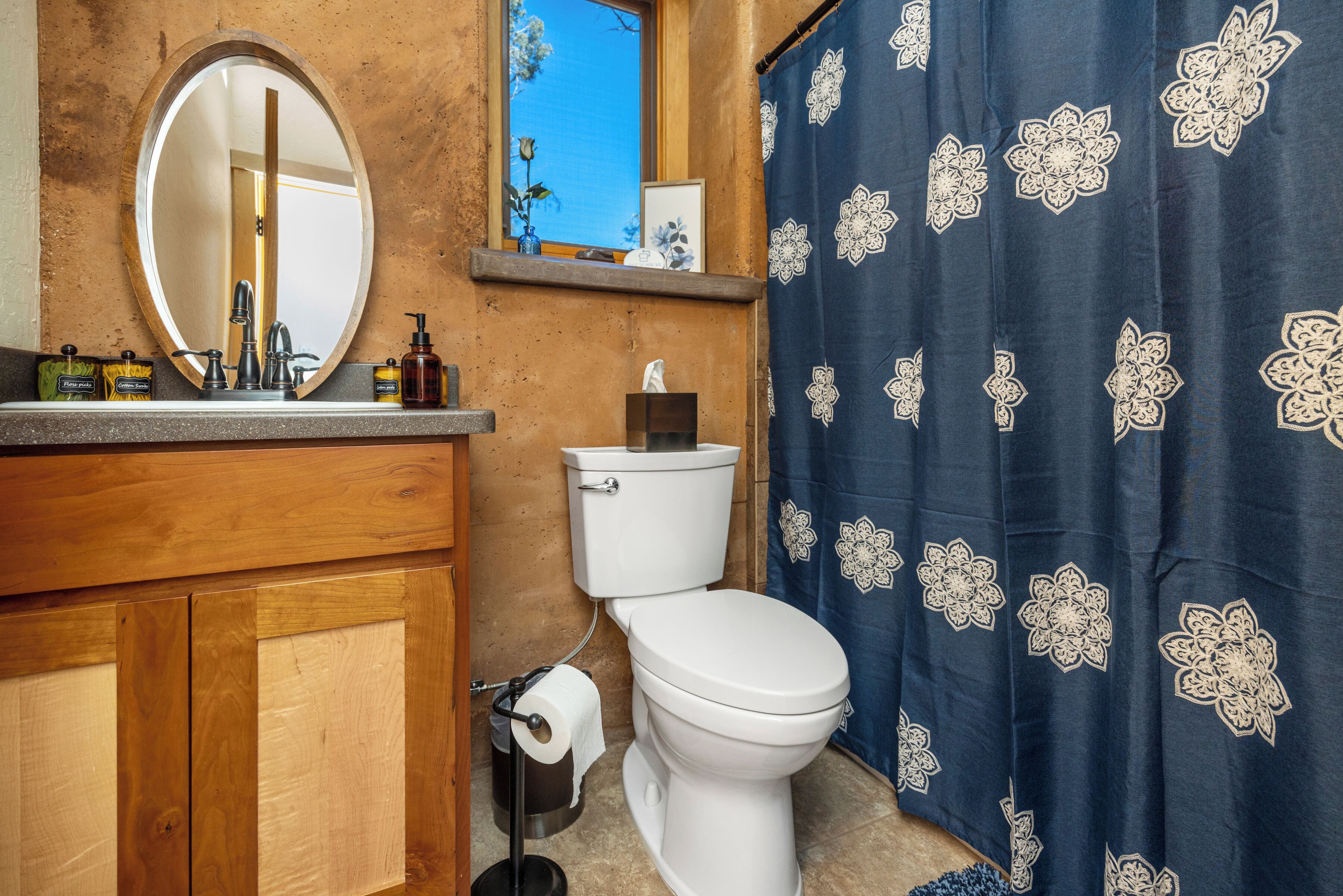 A bathroom with a wooden vanity, a white toilet, a mirror, and a blue shower curtain with floral patterns.