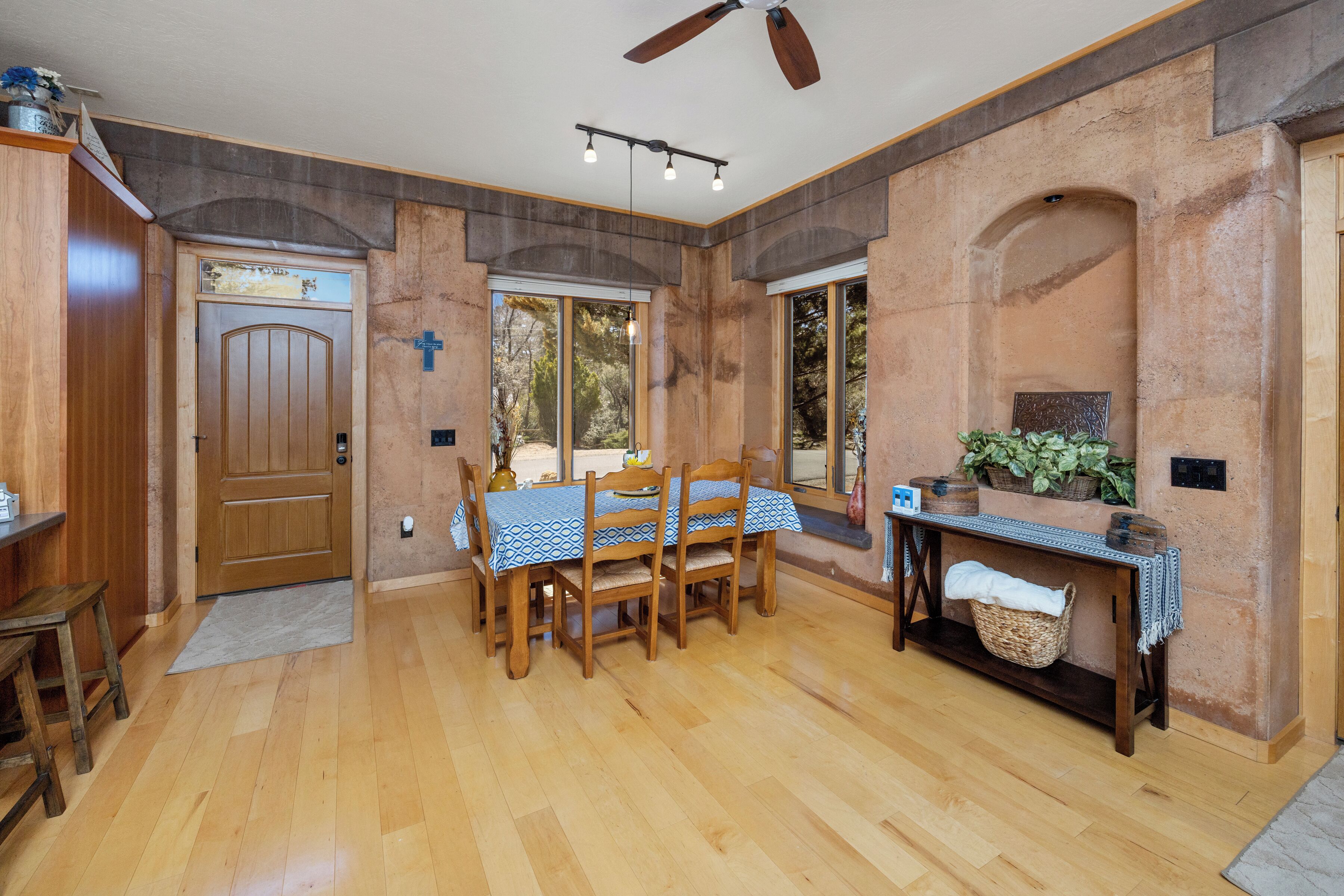 A dining area with a wooden table and chairs, a ceiling fan, and large windows.