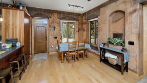 Un comedor con una mesa y sillas de madera, un ventilador de techo y vistas al exterior a través de amplias ventanas.