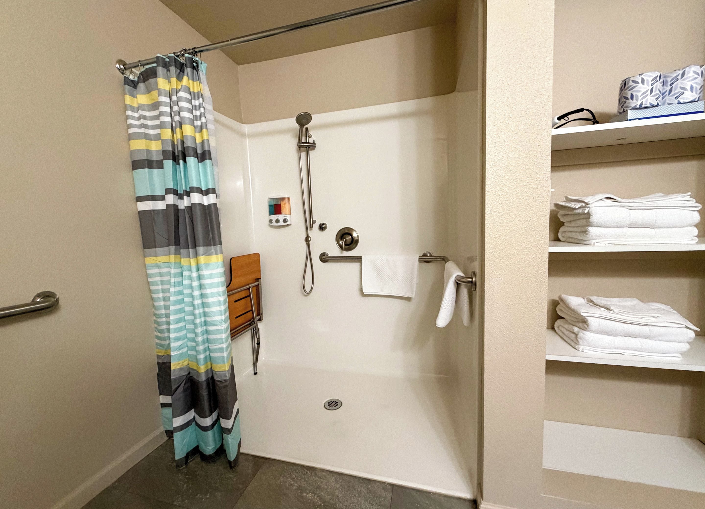 A bathroom with a shower, a towel rack, and a shelf with folded towels.