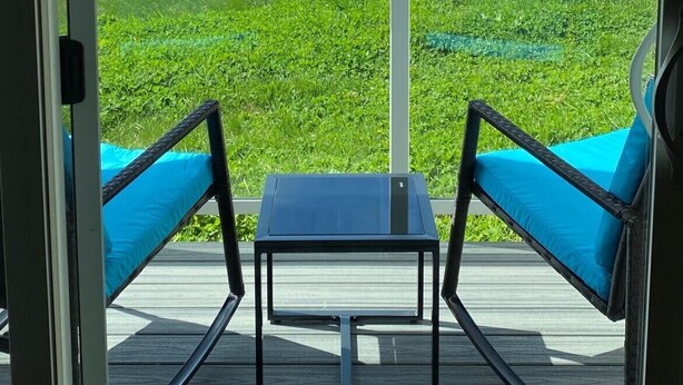A balcony with two blue cushioned chairs and a small table, overlooking a coastal view with a rocky island.