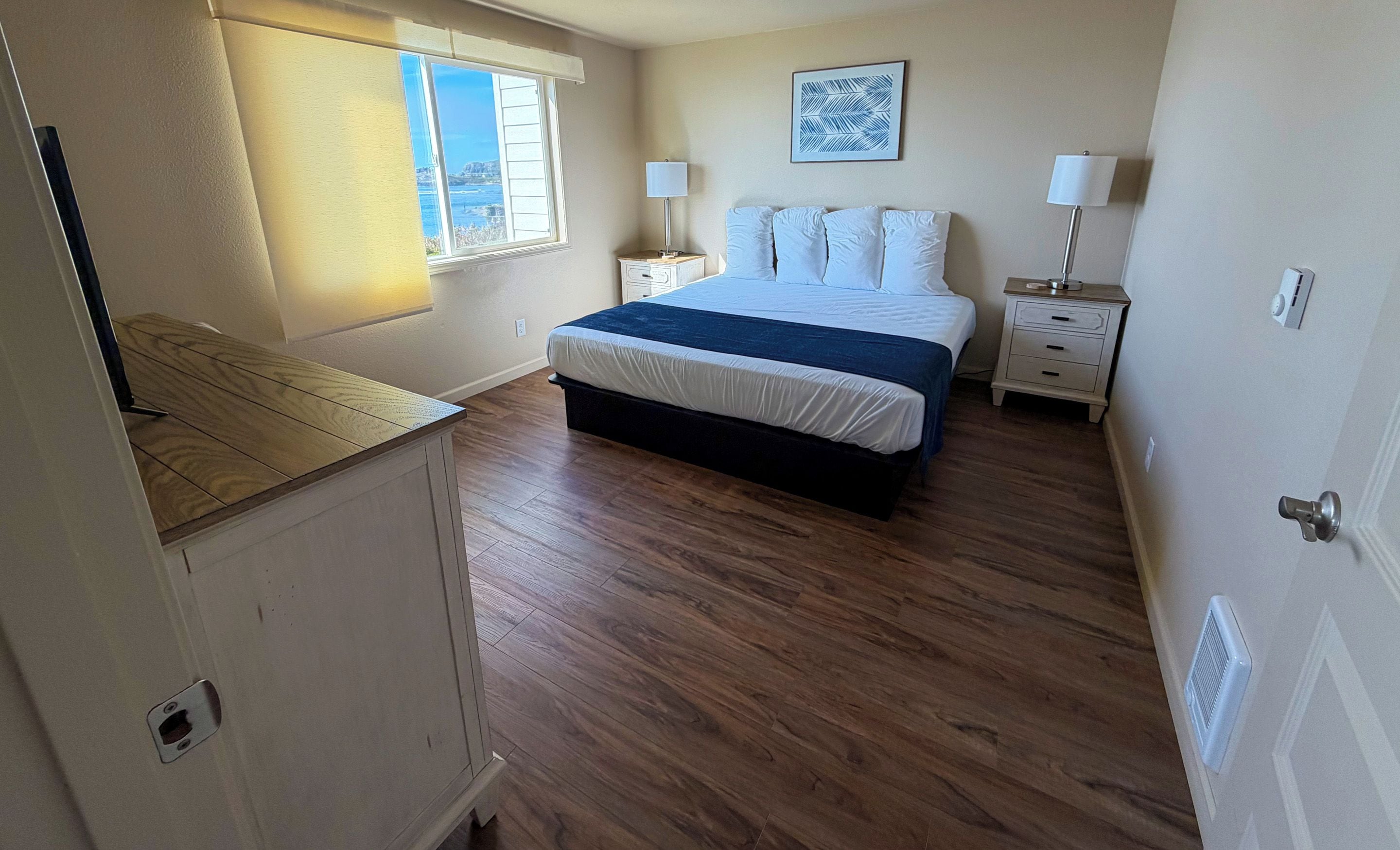 A bedroom with a bed, bedside tables, a window, and a view of the outdoors.