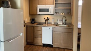 A compact kitchen with a refrigerator, microwave, dishwasher, and wooden cabinets.