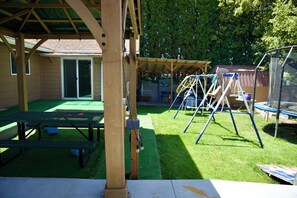 A covered patio area with picnic tables, a swing set, and a trampoline. - Bethesda Inn LLC , Modern, Comfort, Peaceful Stay (Boise)