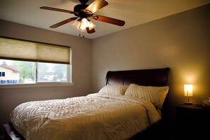 A bedroom with a bed, a ceiling fan, a window with blinds, and a bedside lamp. - Bethesda Inn LLC , Modern, Comfort, Peaceful Stay (Boise)