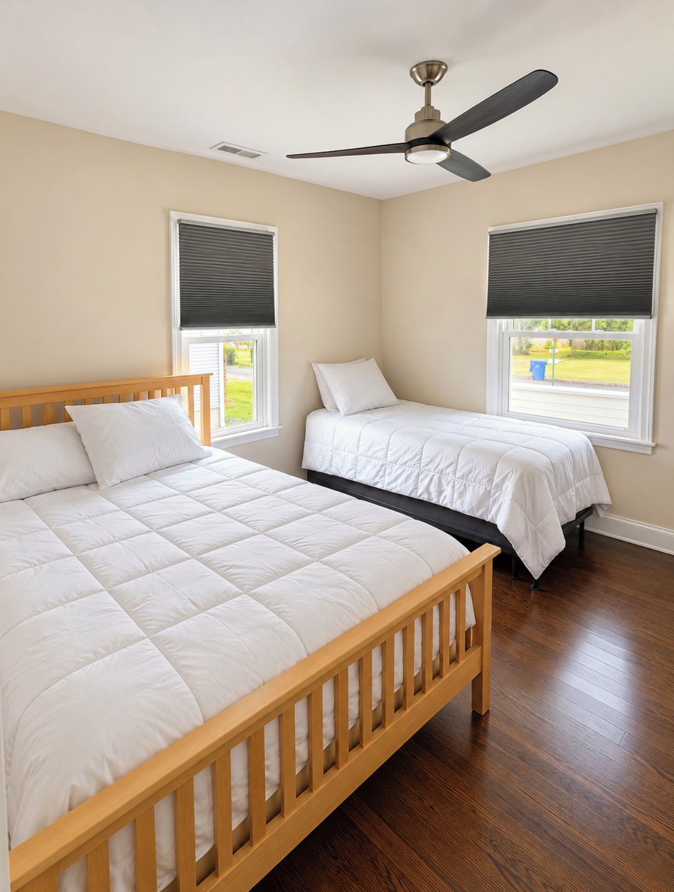 A bedroom with two beds, a ceiling fan, and windows with blinds.