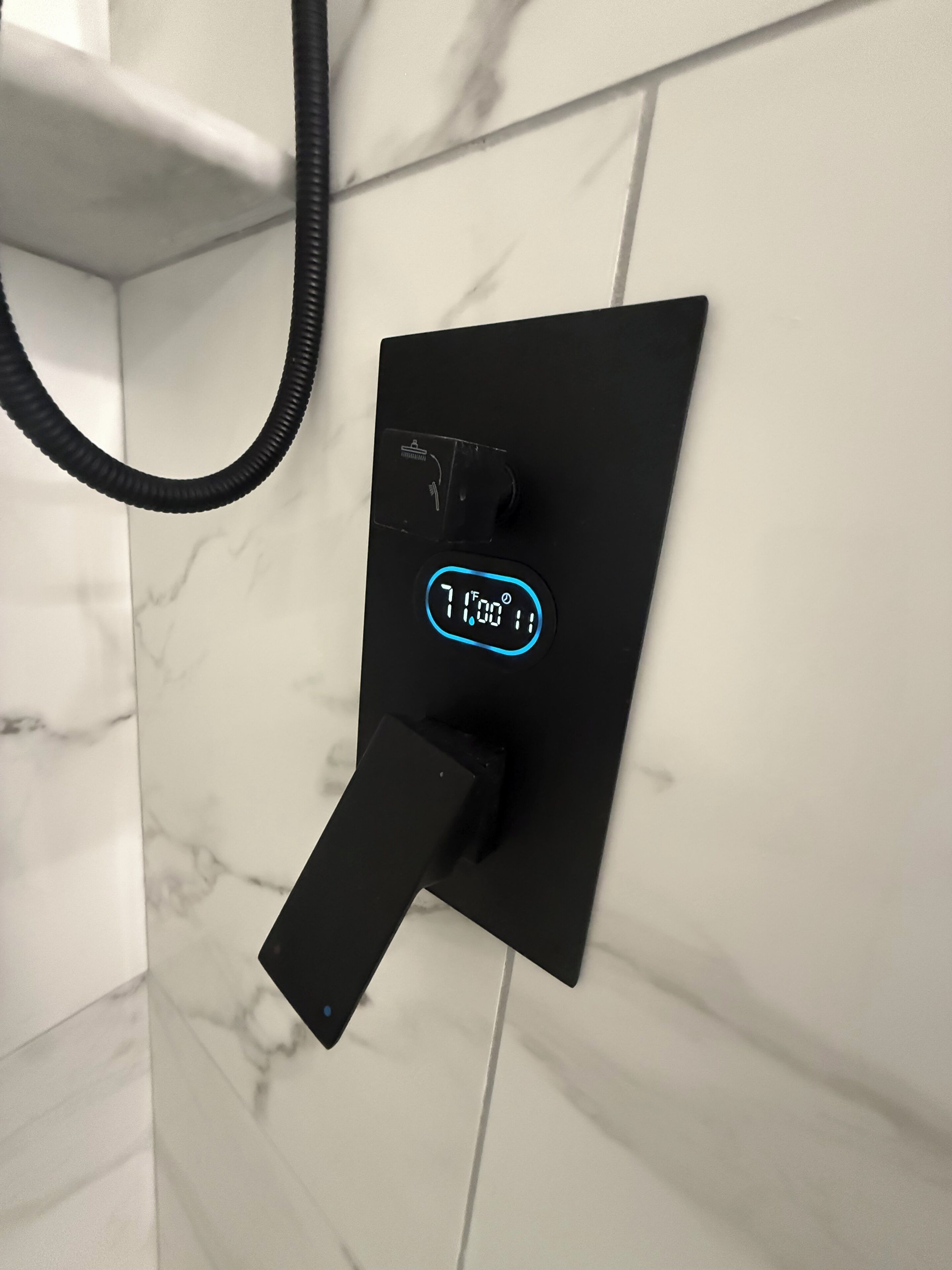 Un termostato digitale nero fissato a una parete rivestita di piastrelle bianche.