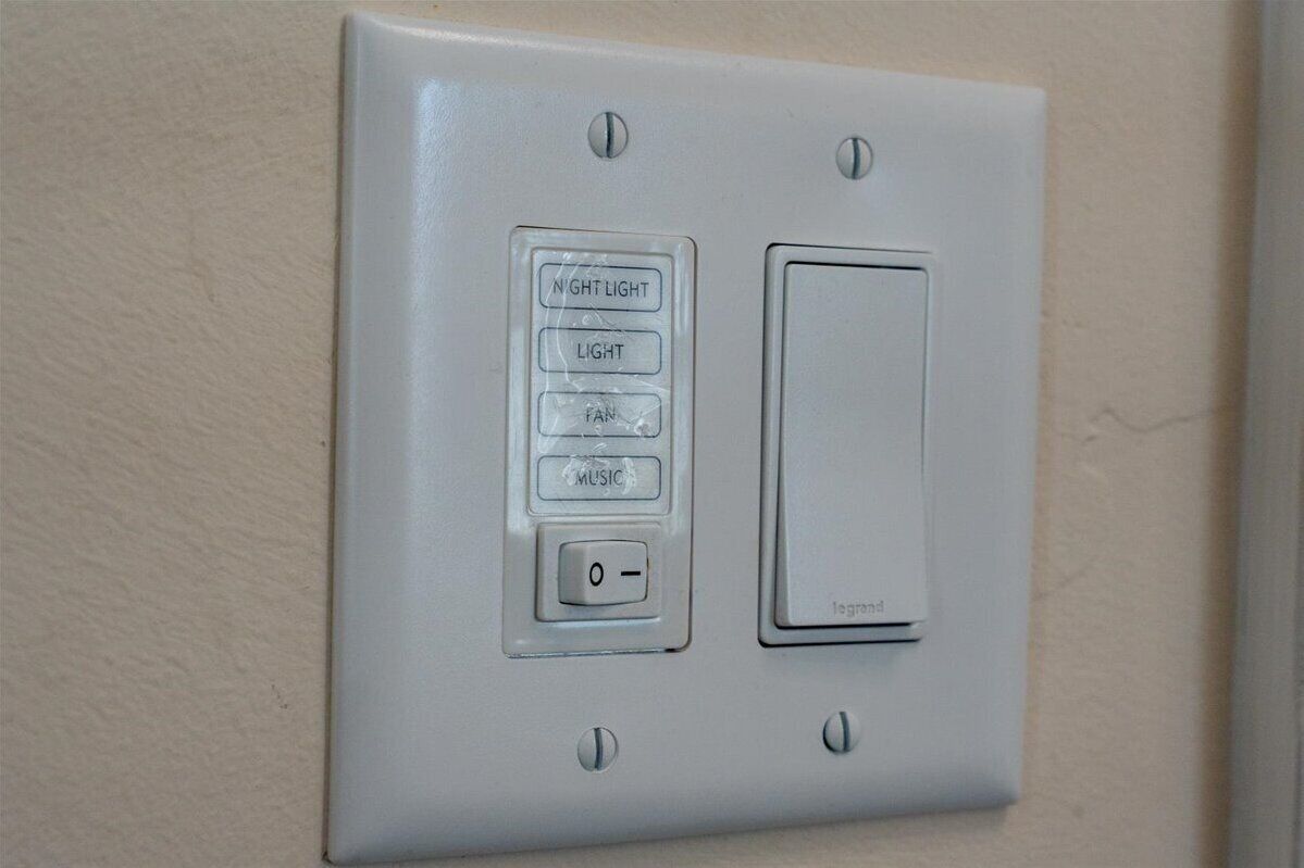 Eine an der Wand montierte Bedienkonsole mit Lichtschalter und einer Taste mit vier Optionen: NACHT, LICHT, VENTILATOR, MUSIK.