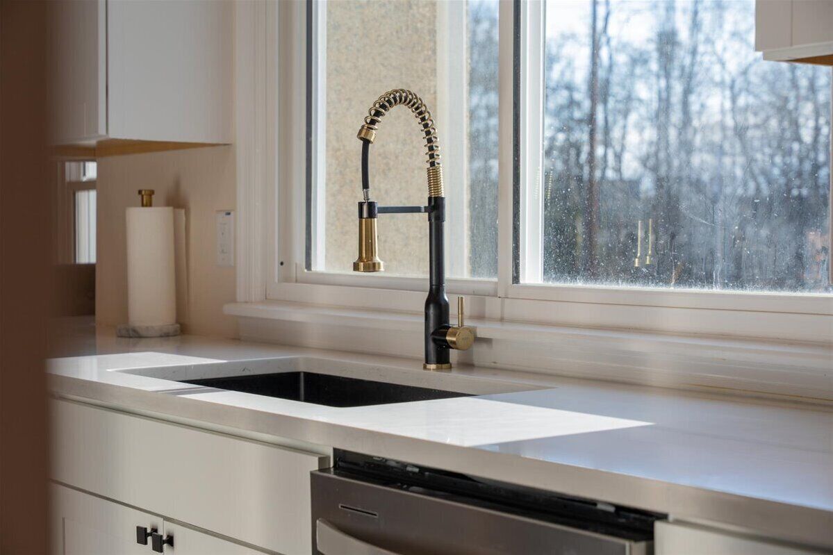 A kitchen with a black sink, a brass faucet, and a window with a view of trees.
