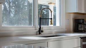A kitchen with a modern faucet, a coffee maker, and a window with a view of trees.