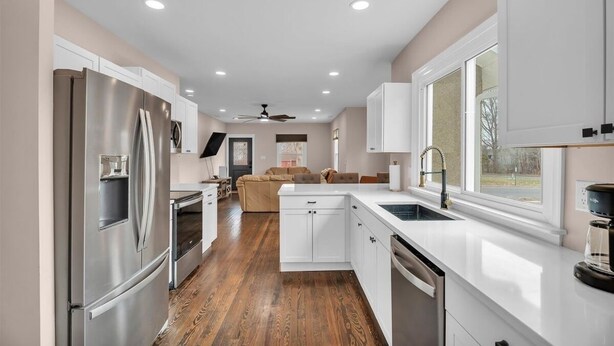 A modern kitchen with white cabinetry, a stainless steel refrigerator, a built-in oven, and a window providing natural light.