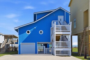Une maison à deux étages, avec une façade bleue, une porte de garage blanche et un balcon doté d’une balustrade.