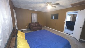 Un dormitorio con cama, una silla, ventilador de techo y televisión.