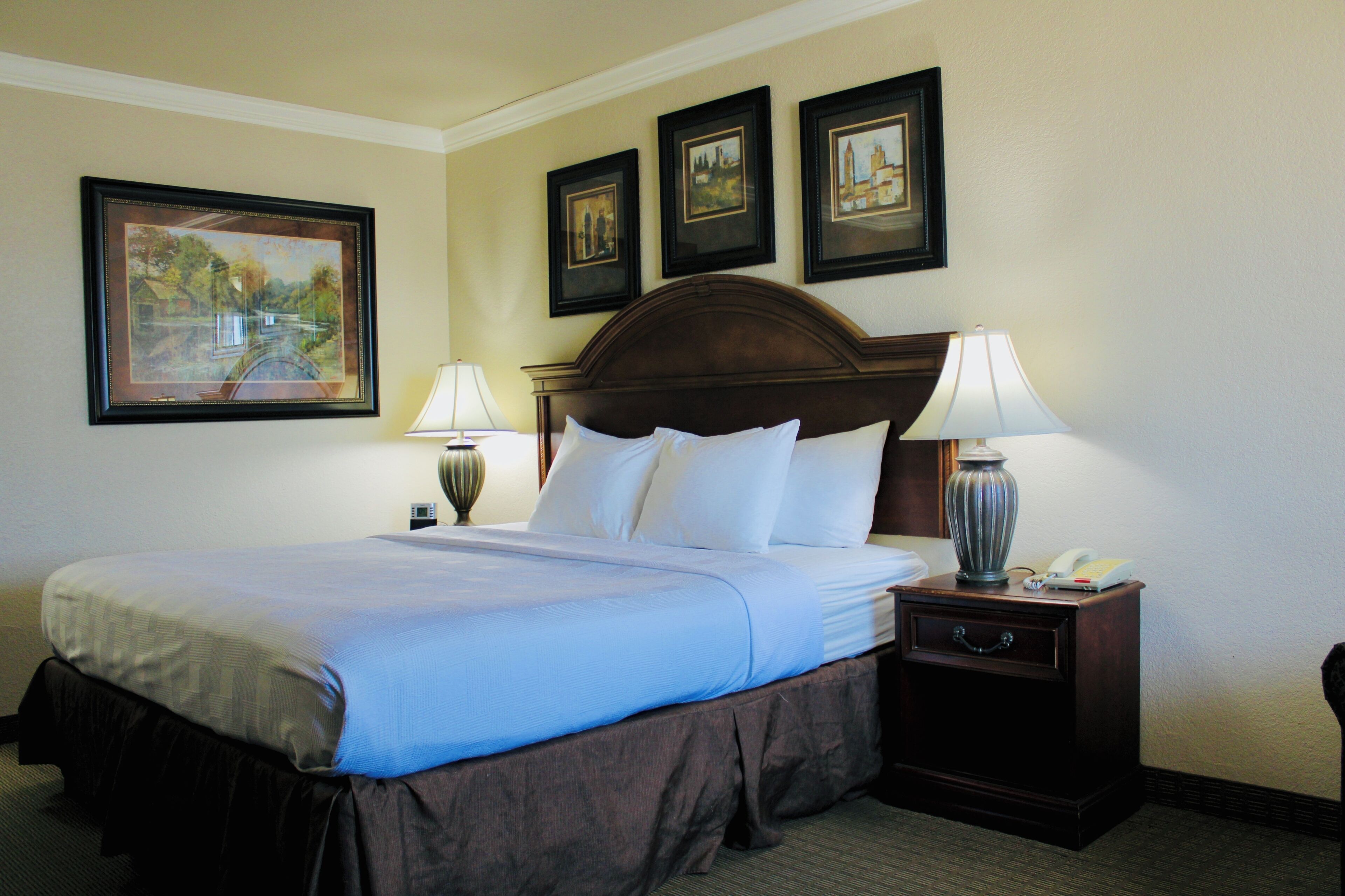A hotel room with a large bed, two bedside tables with lamps, a nightstand with a telephone, and three framed pictures on the wall.