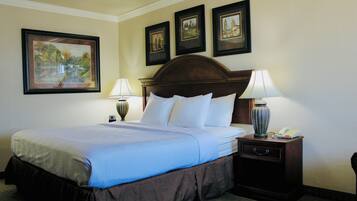 A hotel room with a large bed, two bedside tables with lamps, a nightstand with a telephone, and three framed pictures on the wall.