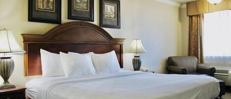 A hotel room with a large bed, two bedside tables with lamps, a chair, and framed pictures on the wall.