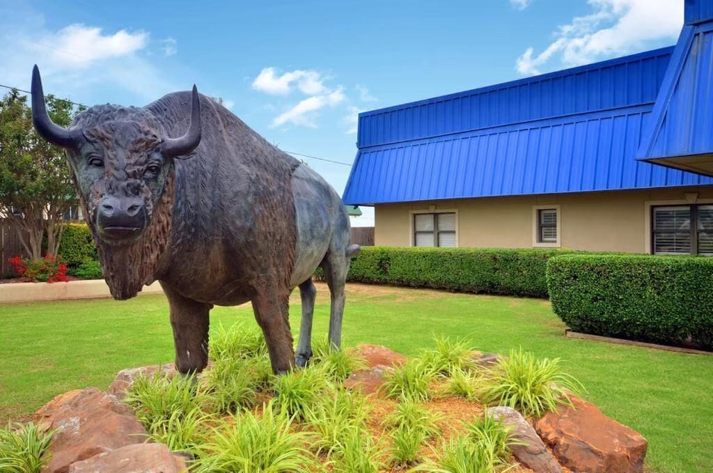 A bull statue in a landscaped garden area with a building featuring a blue roof in the background.