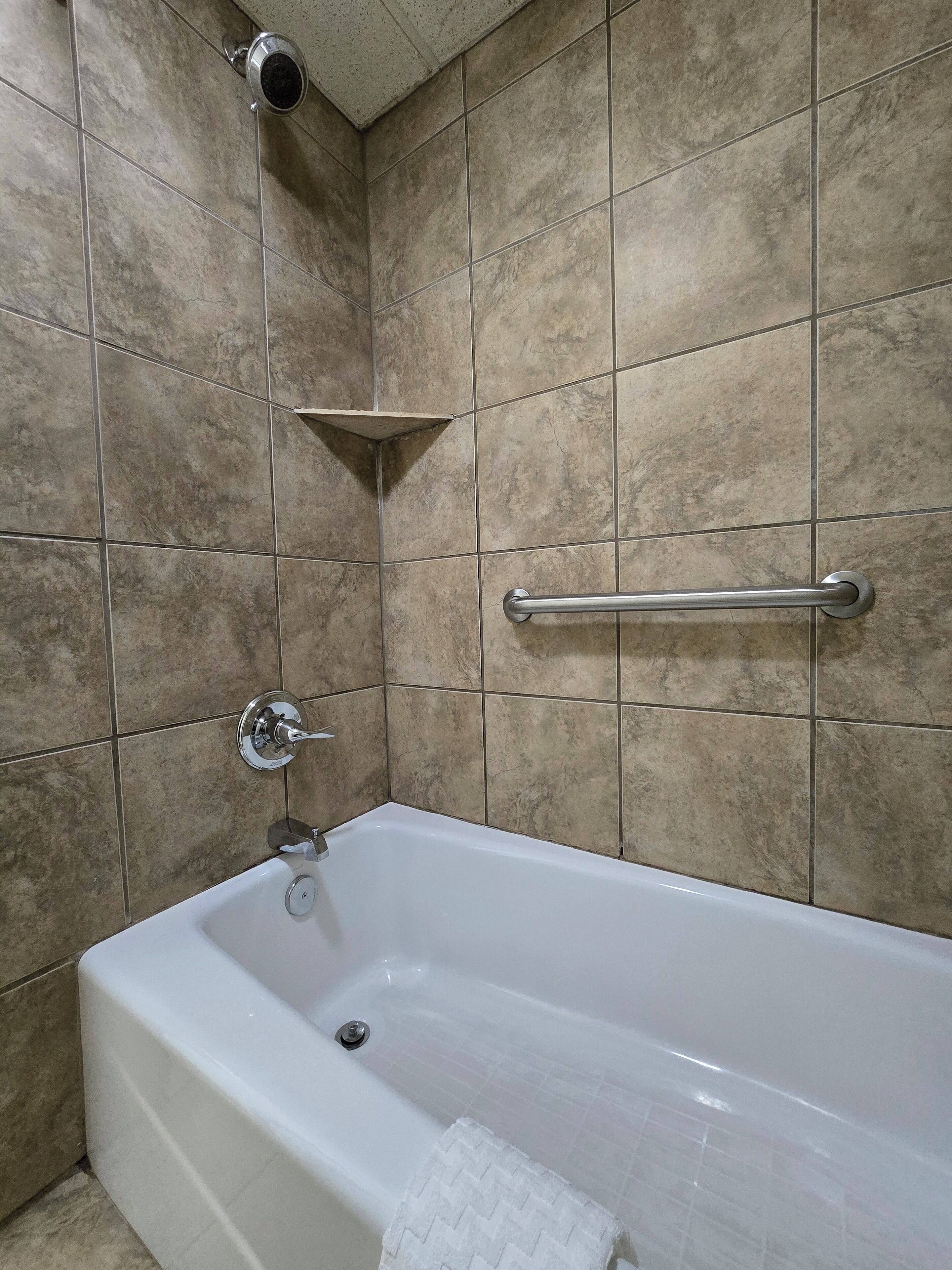 A bathroom with a bathtub, a handrail, and a towel rack.