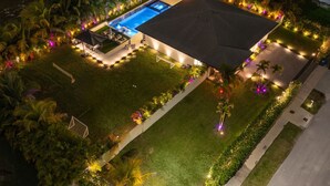 Vista aérea de una propiedad residencial bien iluminada con piscina, terraza cubierta y jardines ajardinados.