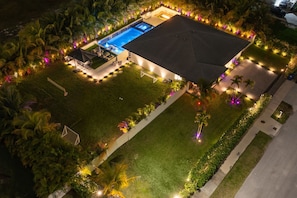 Eine Vogelperspektive auf ein gut beleuchtetes Wohnhaus mit Swimmingpool, einer überdachten Terrasse und angelegten Gärten.