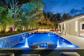 Una piscina con cascada, rodeada de palmeras y mobiliario de exterior.