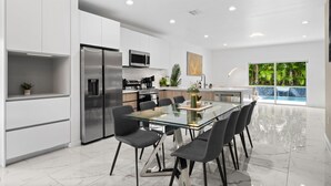 Una cocina moderna con mesa de comedor de vidrio, electrodomésticos de acero inoxidable y vistas a una piscina.