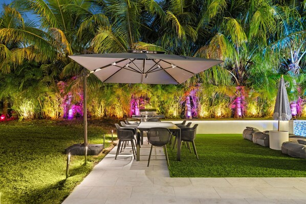 Un área de comedor al aire libre con una mesa y sillas, rodeada de abundante vegetación y palmeras.