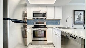 Una cocina moderna con electrodomésticos de acero inoxidable, armarios blancos y un salpicadero azul.
