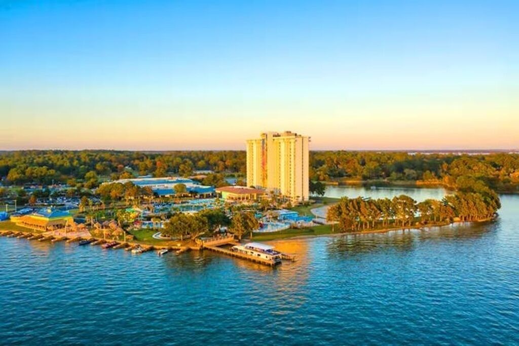 A high-rise hotel with a waterfront view, surrounded by greenery and a lake.