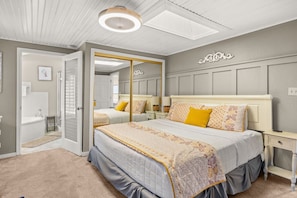 A bedroom with a large bed, bedside tables, a mirror, and a bathroom visible through an open door.