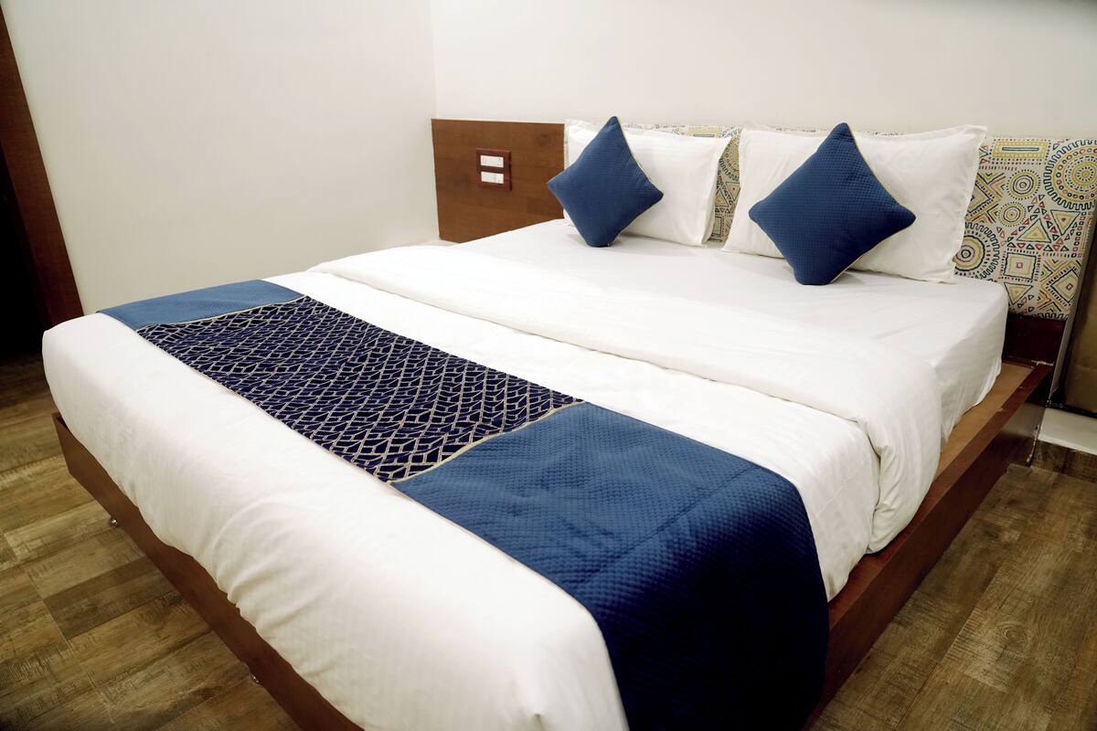 A neatly made bed with a white and blue bedspread, two blue pillows, and a wooden headboard.