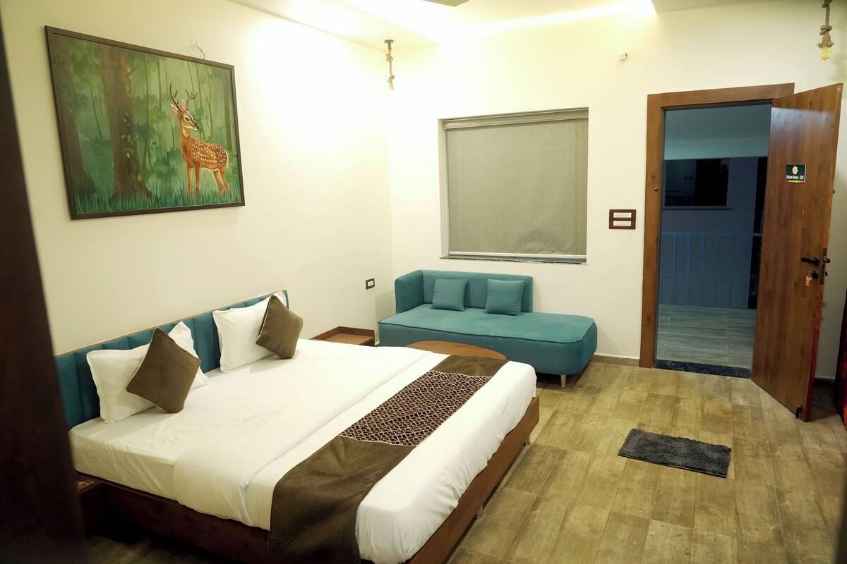 A bedroom with a bed, a sofa, a painting of a deer, a window, and a door.