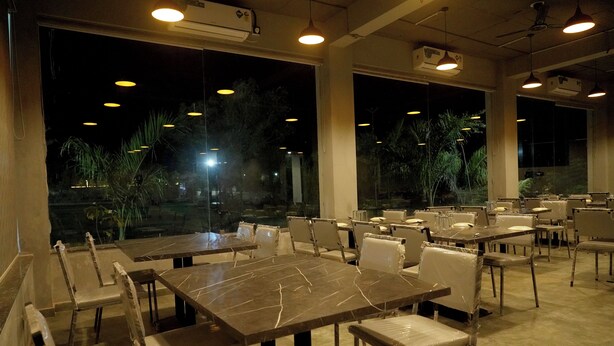 A restaurant with multiple tables and chairs, large windows, and hanging pendant lights. - Sonchafa Resort Pauni (Pawni)